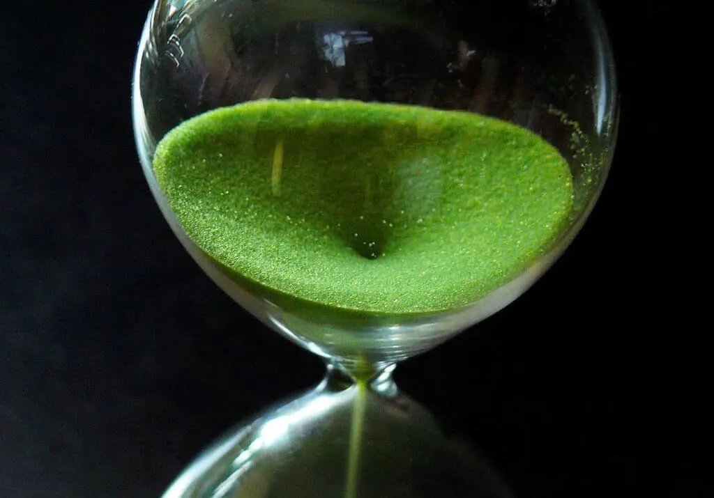 closeup of hourglass with green sand; time running out concept