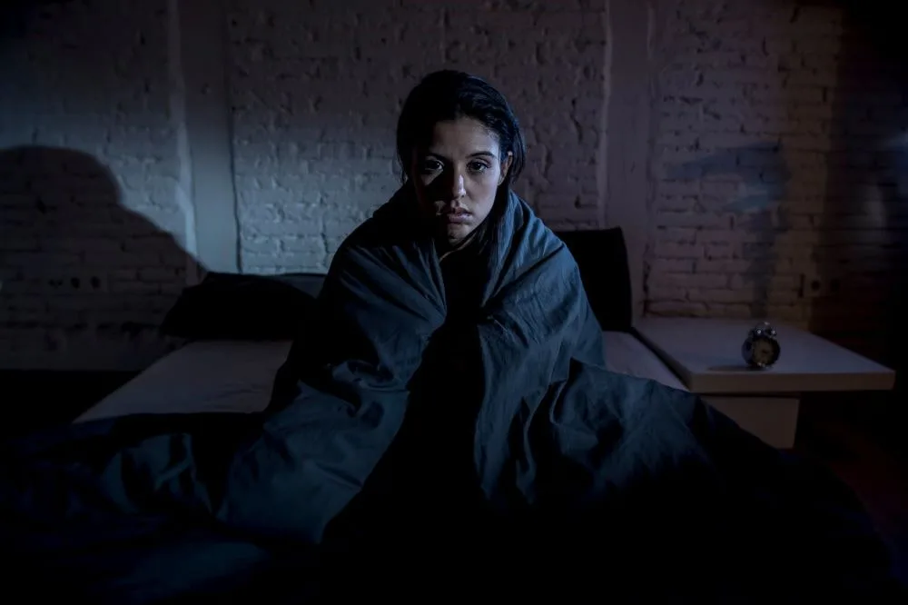 Woman covered in a thick blanket sitting inside a dark room