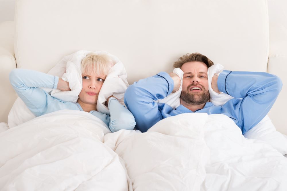 Couple Covering Ears While laying On Bed At Home