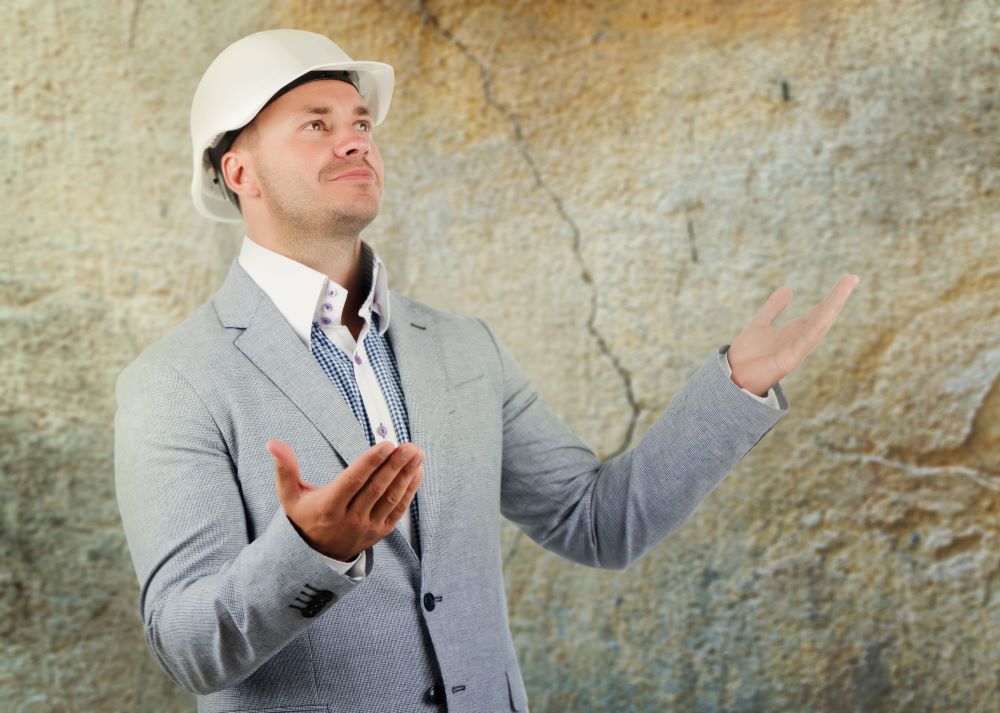 Engineer pleading ignorance or a crack in a wall behind him raising his hands to show he doesn't know what happened