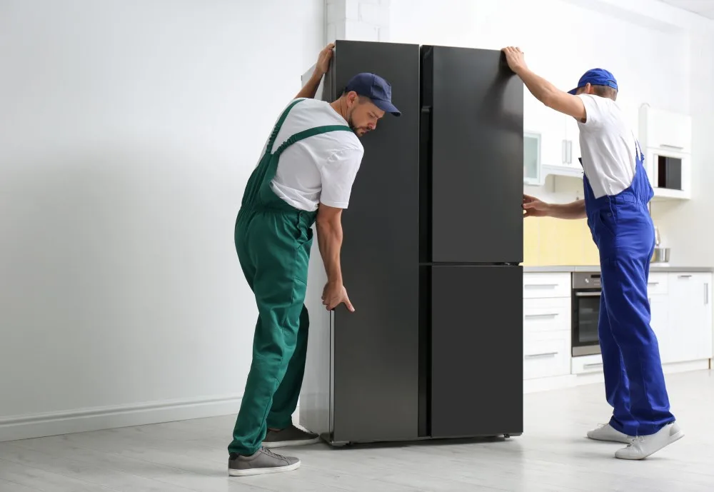 Professional workers carrying modern refrigerator in kitchen