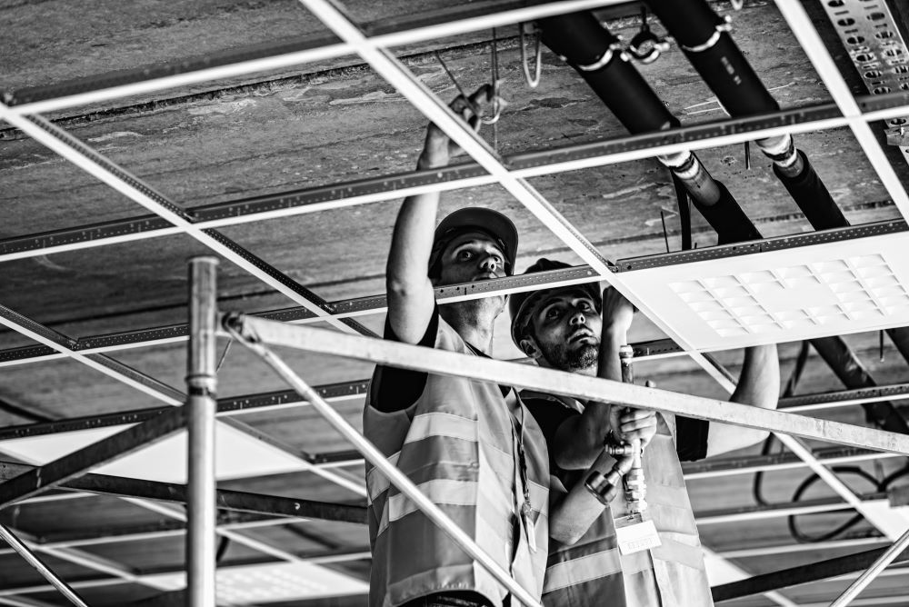 Installation workers working on construction site; pipe and ductwork over suspended ceiling