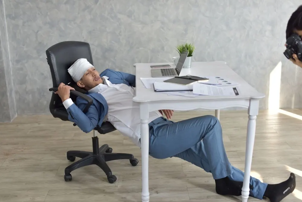 Overworked businessman with bandaged hurt head in front of scattered papers or documents