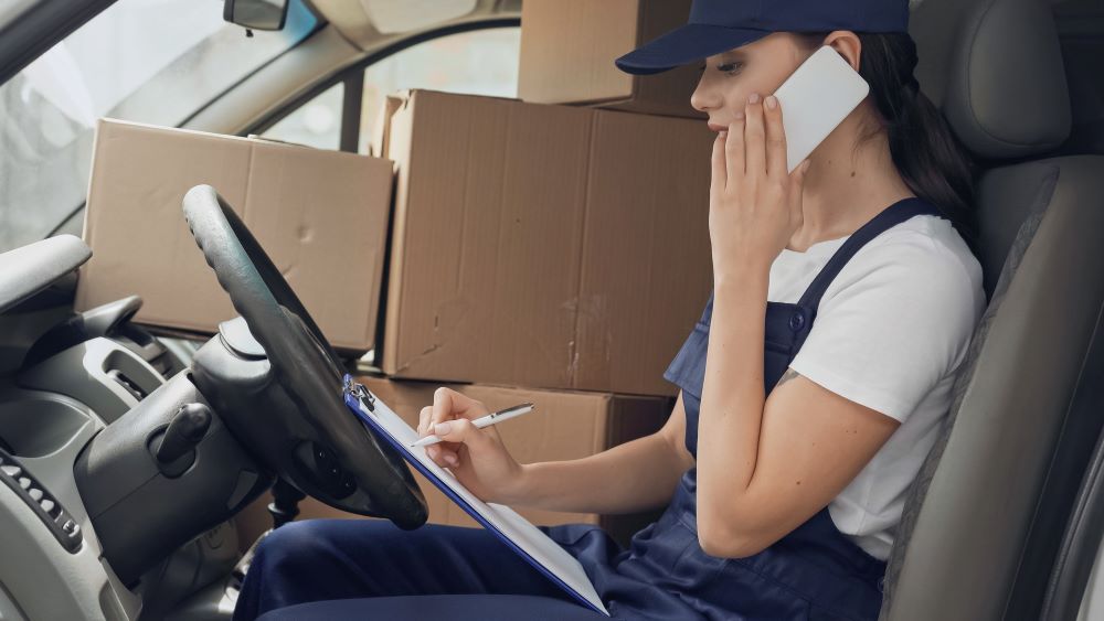 Side view of delivery woman talking on smartphone and writing; uber driver; boxes inside a vehicle