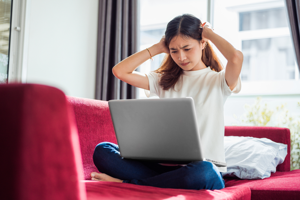 Asian young exhausted businesswoman having headache while using laptop on  sofa in her house. Business people worry and stress about job deadline concept. Online shopping marketing technical problem