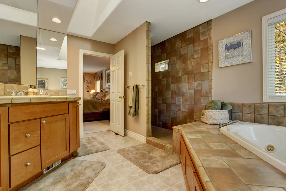 Spacious bathroom with tile wall trim and corner bath tub. View of bathroom vanity cabinet
bath mats, bath rugs
