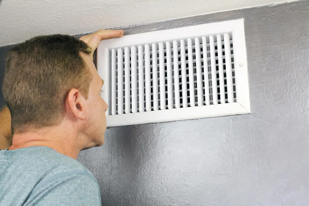Mature man examining an outflow air vent grid and duct to see if it needs cleaning. One guy looking into a home air duct to see how clean and healthy it is.

man looking at vents