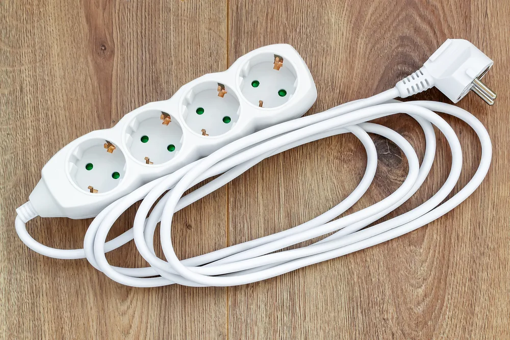 White four outlets power extension cord on a wooden surface. New electric power strip for home or office. Household appliances. Top view.
extension wire