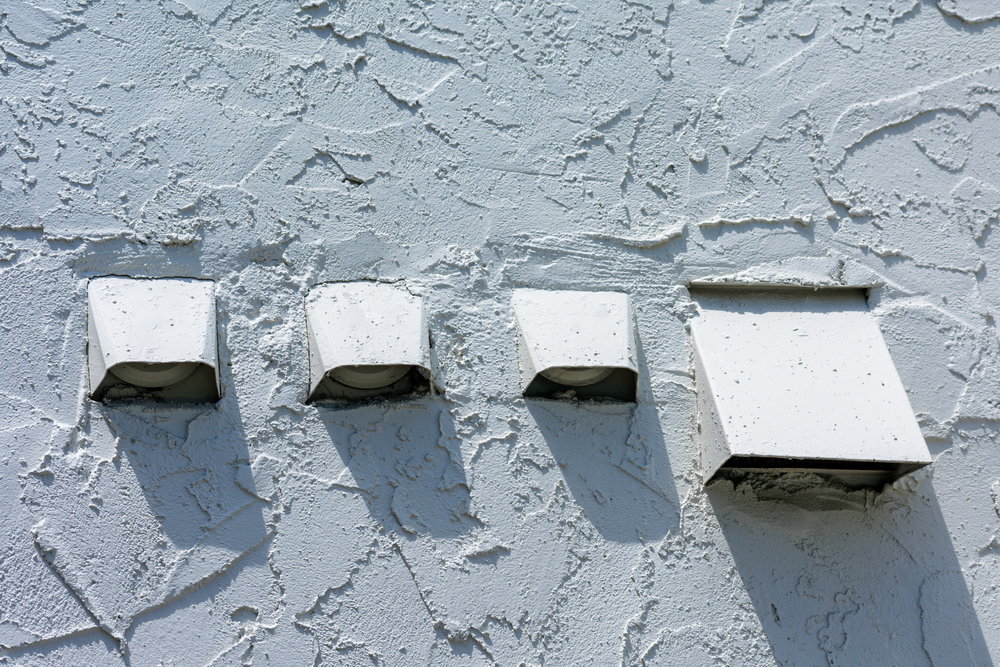 Several air exhaust vents with flapper and screen on white stucco wall of residential building