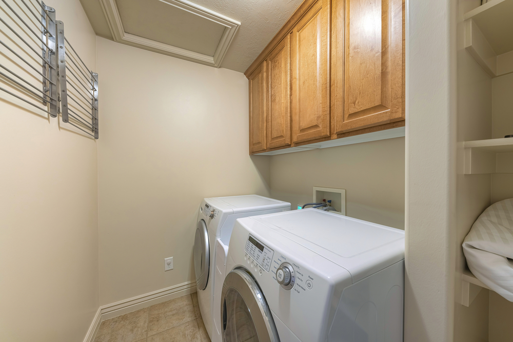Small laundry room interior with wall-mounted drying rack. There are laundry appliances on the right below the wooden wall cabinets on the right.