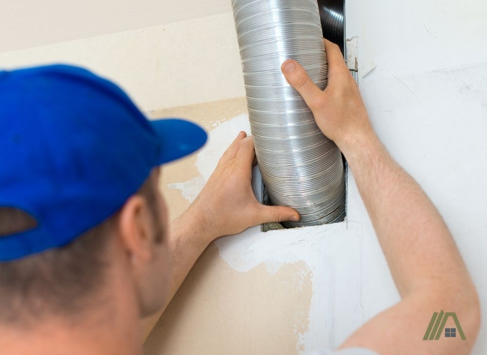 Man wearing blue hat installing flexible duct inside a wall