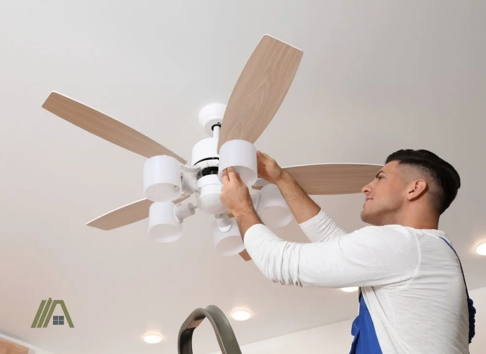 man replacing the light bulb of a ceiling fan