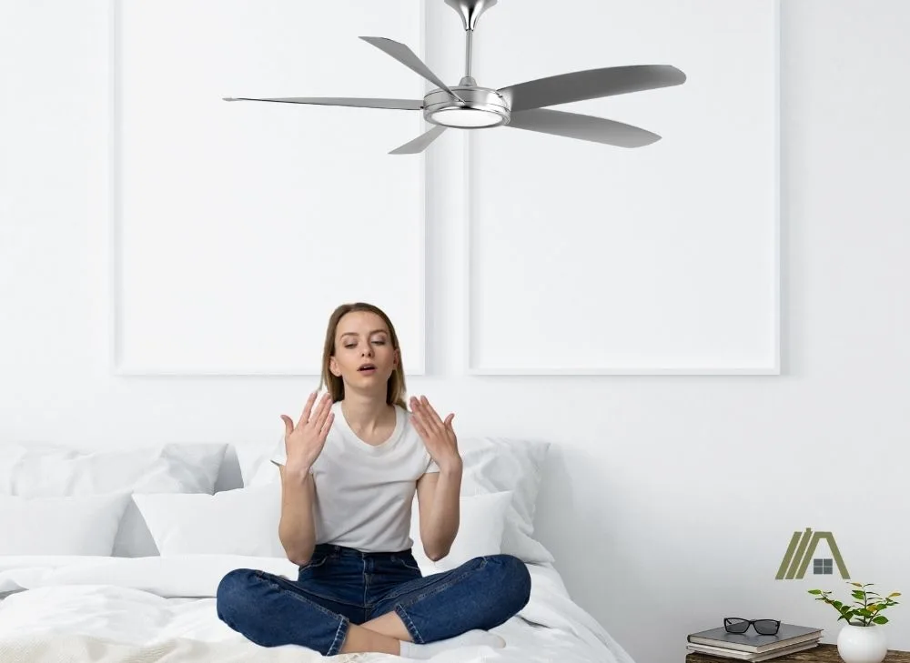 sweaty woman sitting in bed with ceiling fan on