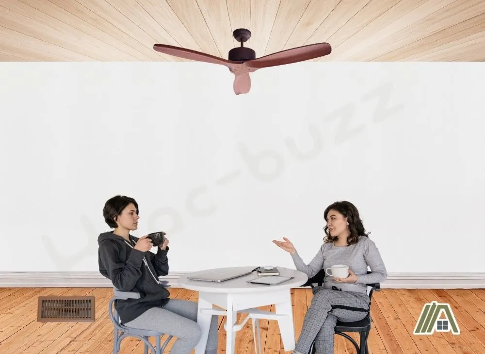 Women talking under a ceiling fan with a floor register on the side