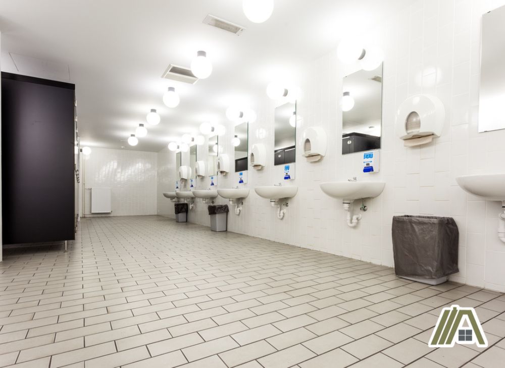 Washroom with white tiles, toilet, sink and bright lights