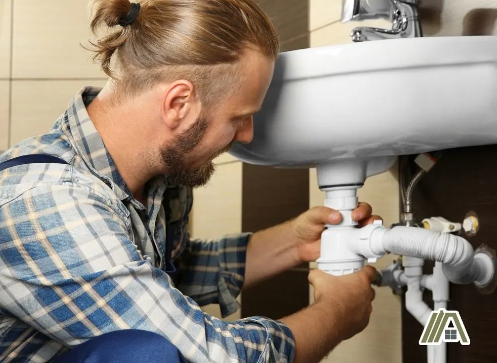 Blonde man in a bun fixing the drain pipe of the faucet