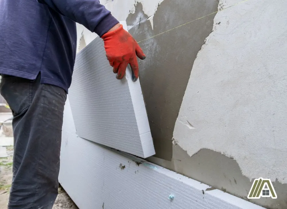 Man wearing gloves installing a foam board insulation on a concrete wall