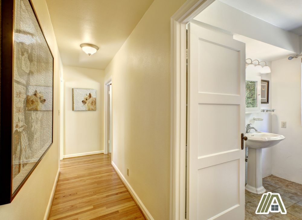 Cream colored hallway walls with a bathroom on the end leading to it