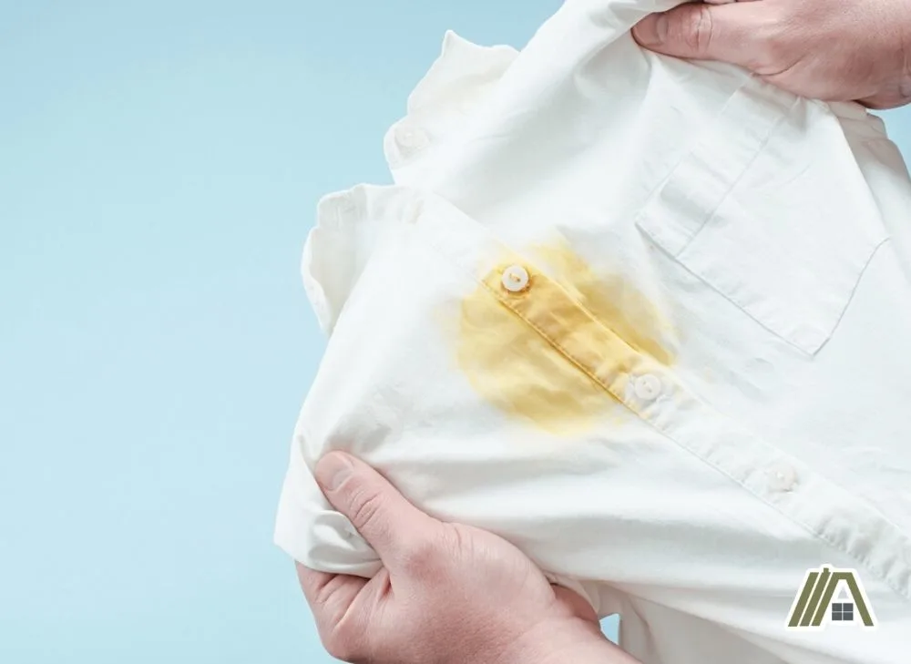 Man holding a white polo shirt with yellow stain on it