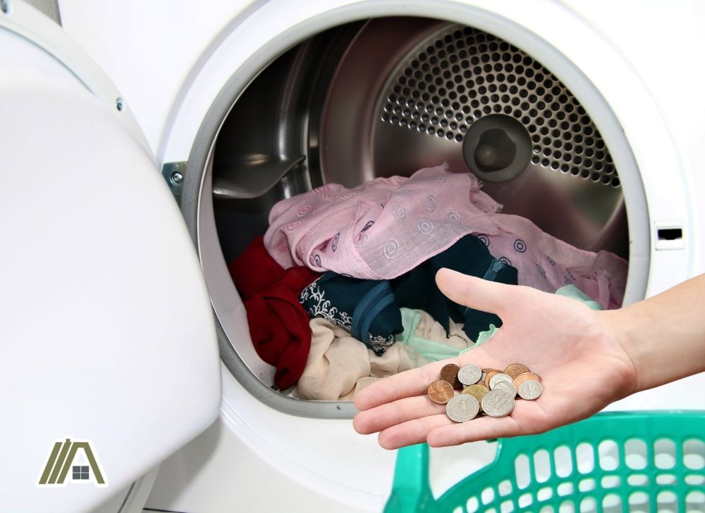 Open dryer with clothes, man with coins in his hand from the dryer