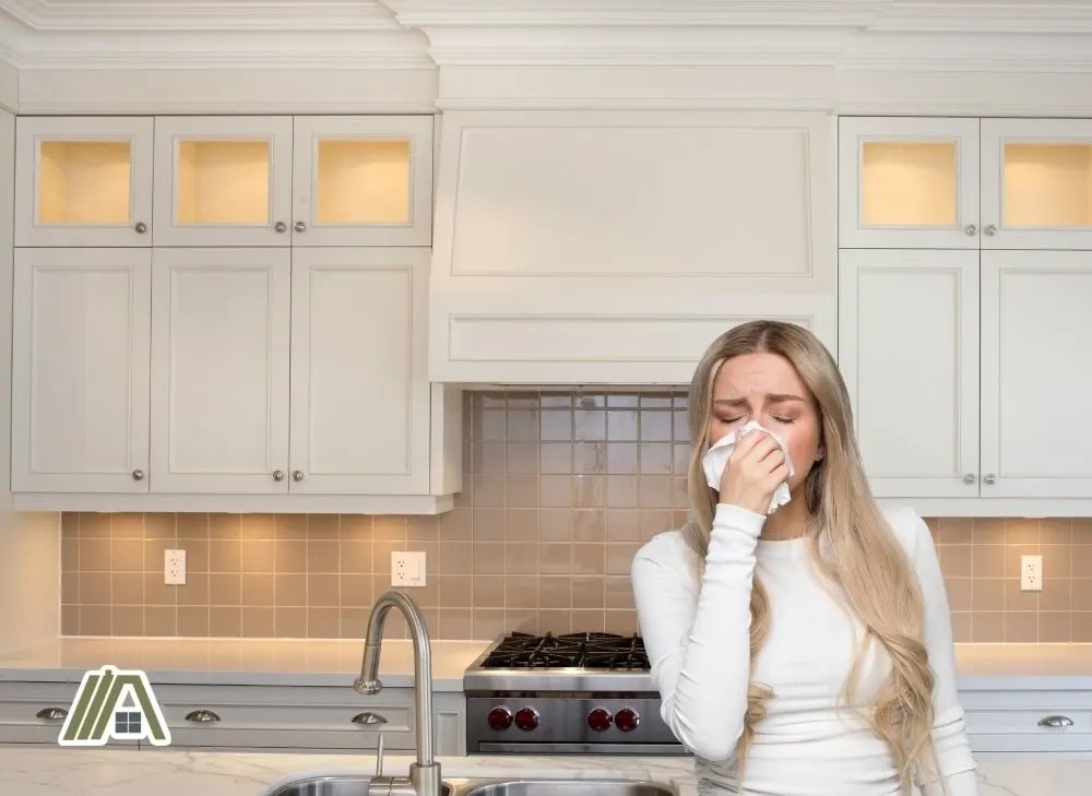 Woman sneezing in the kitchen with white cupboards