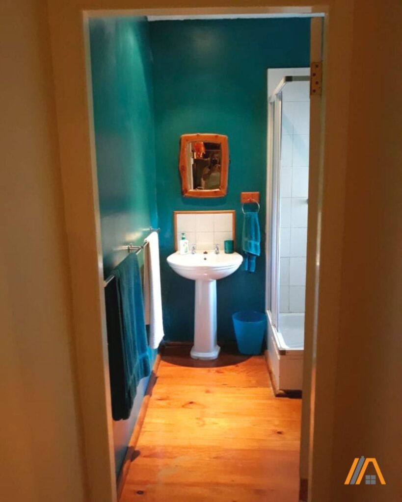 Old bathroom style with sink and shower cubicle with turquoise wall and yellow wooden floor.jpg