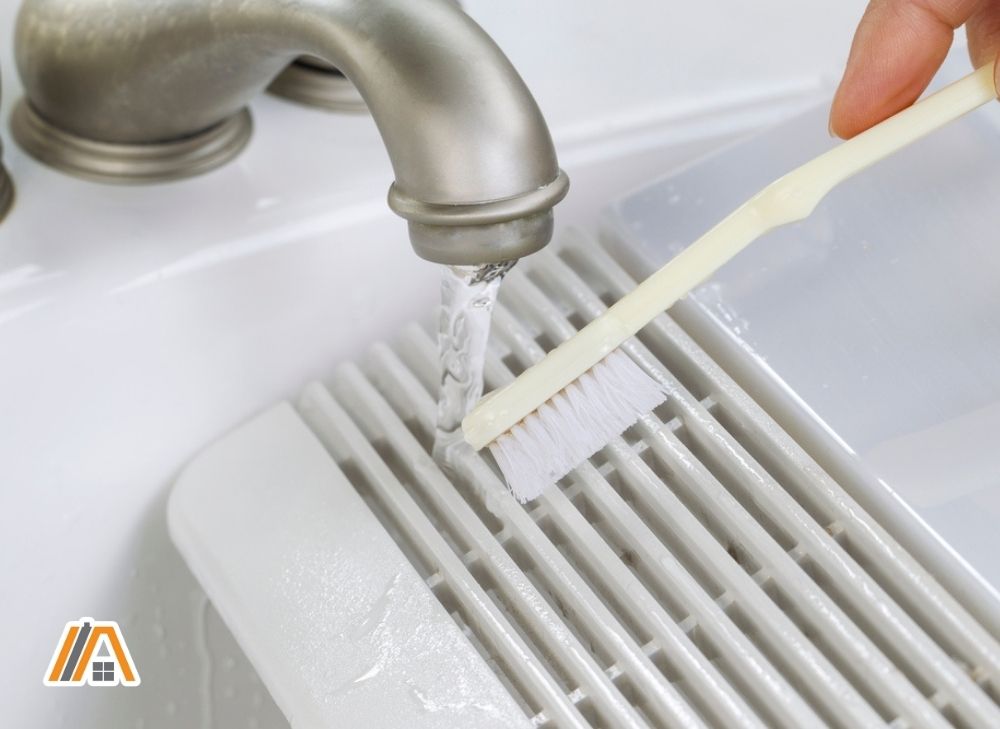 Cleaning the bathroom exhaust fan cover in the sink using a toothbrush