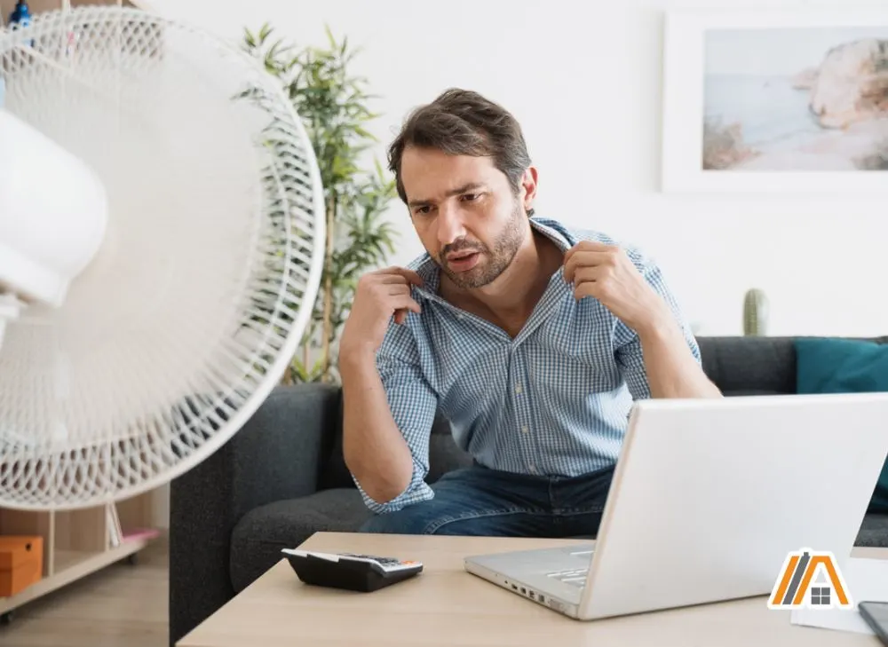Man feeling hot sitting in the living room while the fan is pointed at him