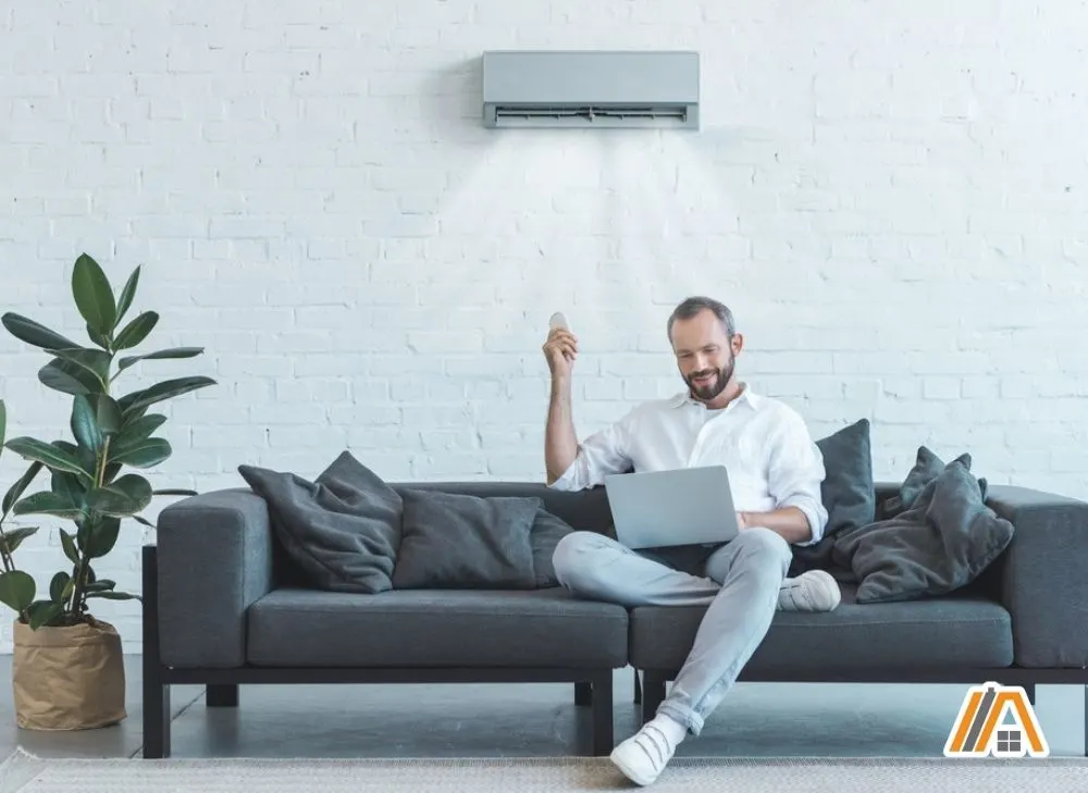 Man-using-his-laptop-while-turning-on-the-air-conditioning-in-the-modern-living-room