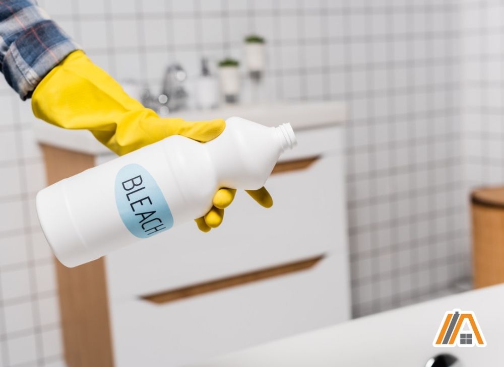 Woman wearing yellow gloves holding a bleach in the bathroom